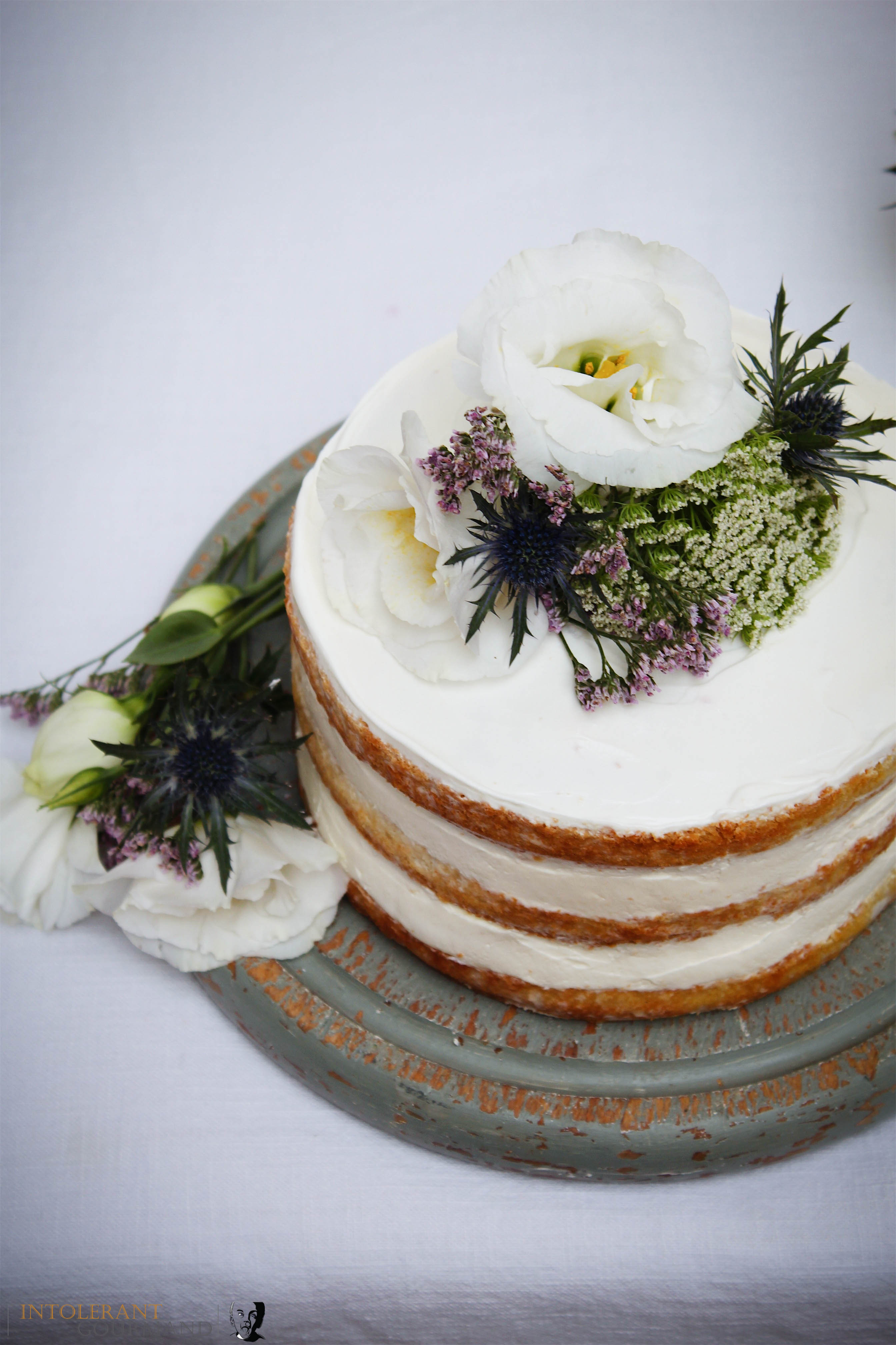 Royal Wedding Cake - Elderflower and Lemon. A beautiful 3 tiered naked cake, covered with smooth buttercream and finished off with fresh flower decorations. Flavoured with elderflower and lemon and perfect for any celebration! It is also gluten-free! www.intolerantgourmand.com