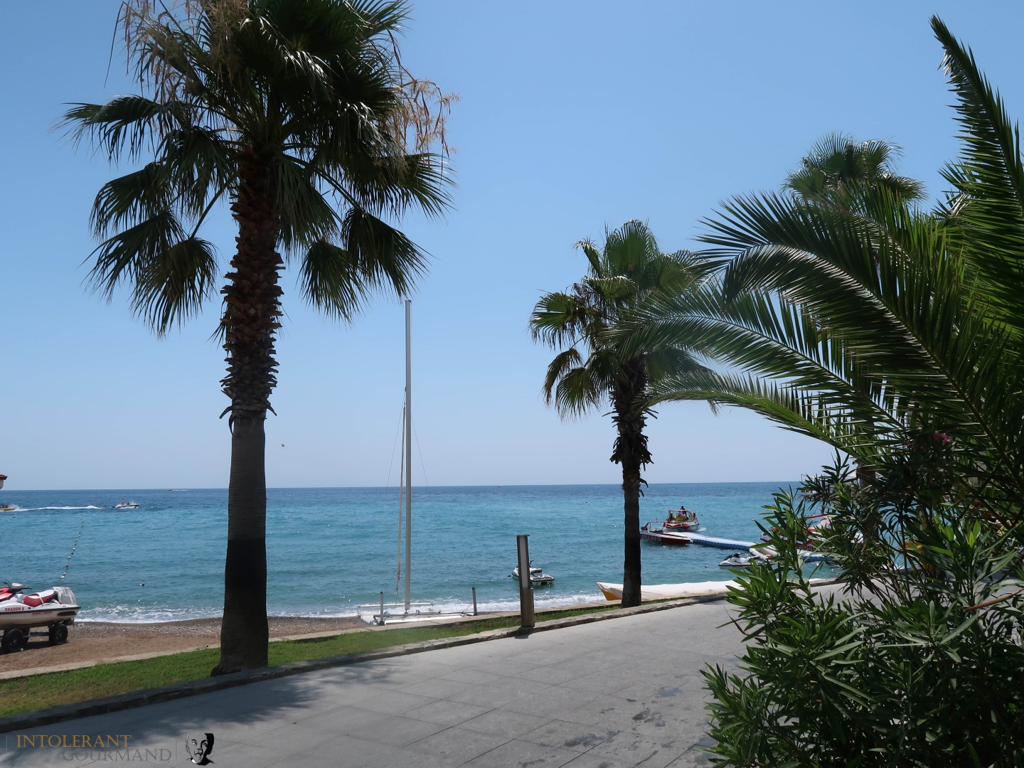 Rixos Sungate Kemer Antalya with Jet 2 Holidays - beach photo, palm trees, and blue skies with the sea in the background. www.intolerantgourmand.com